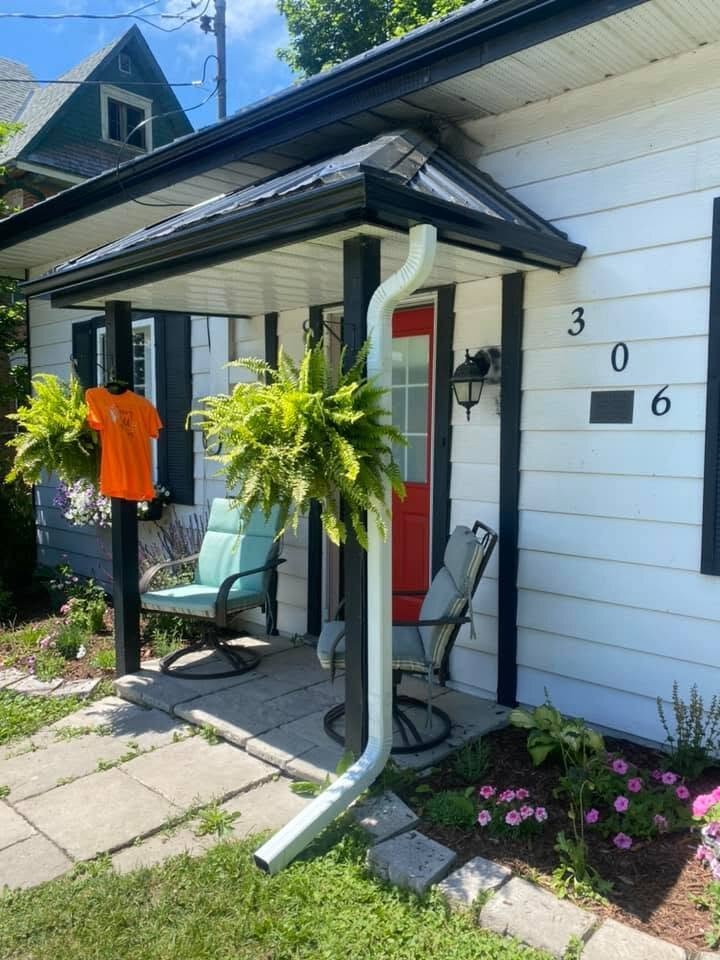 Black seamless eavestrough and downspout on a white-sided home with a covered porch.