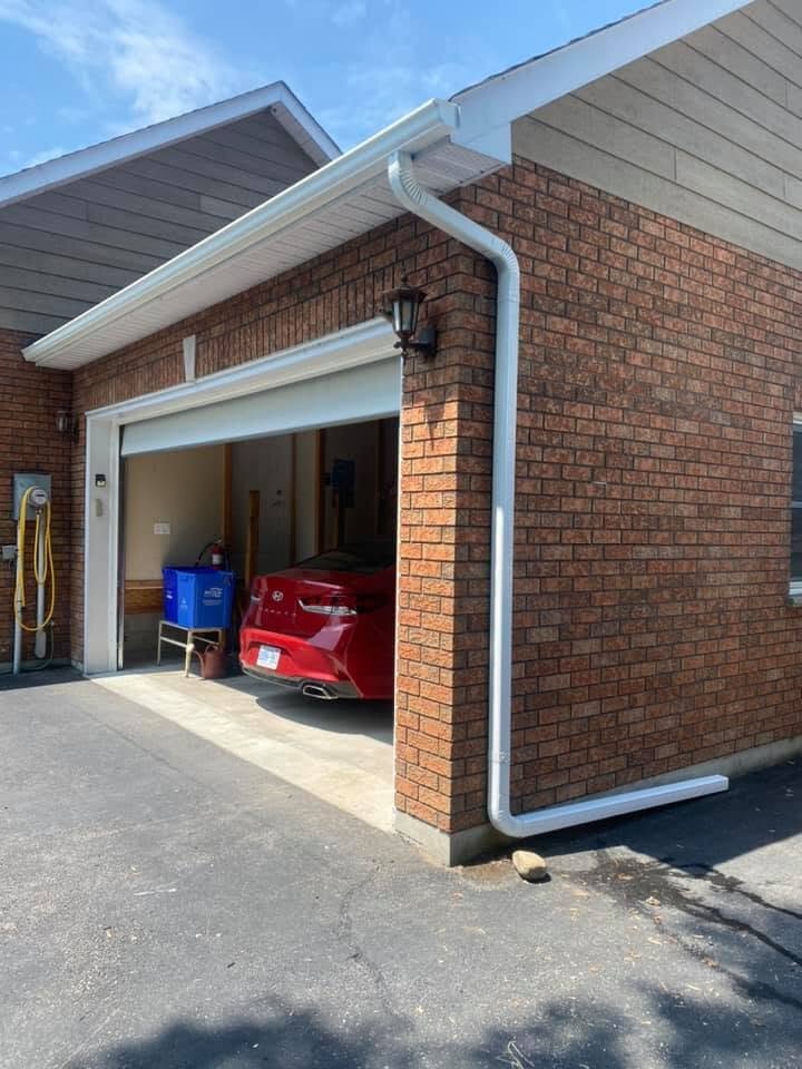 New white downspout installed at the corner of a brick garage.