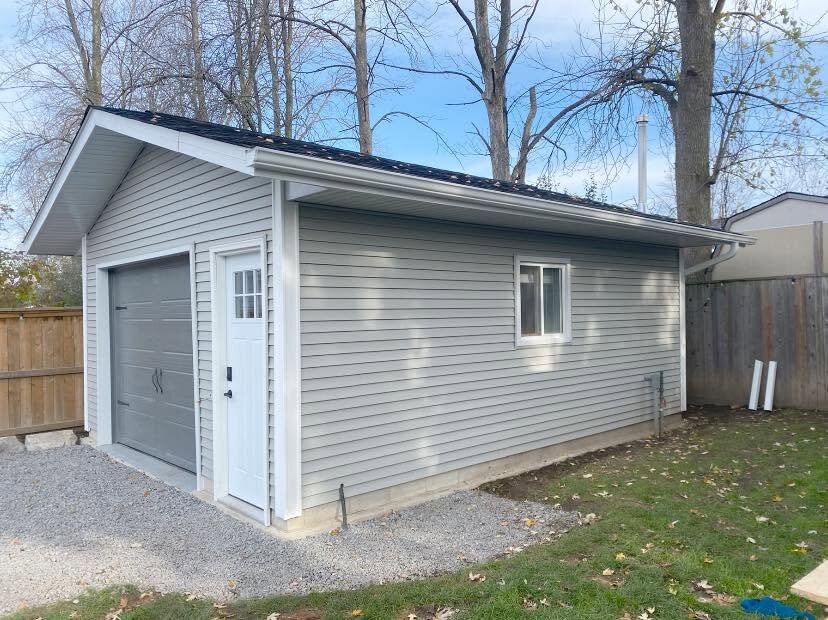 Detached garage with new light siding, white eavestrough, and grey door.