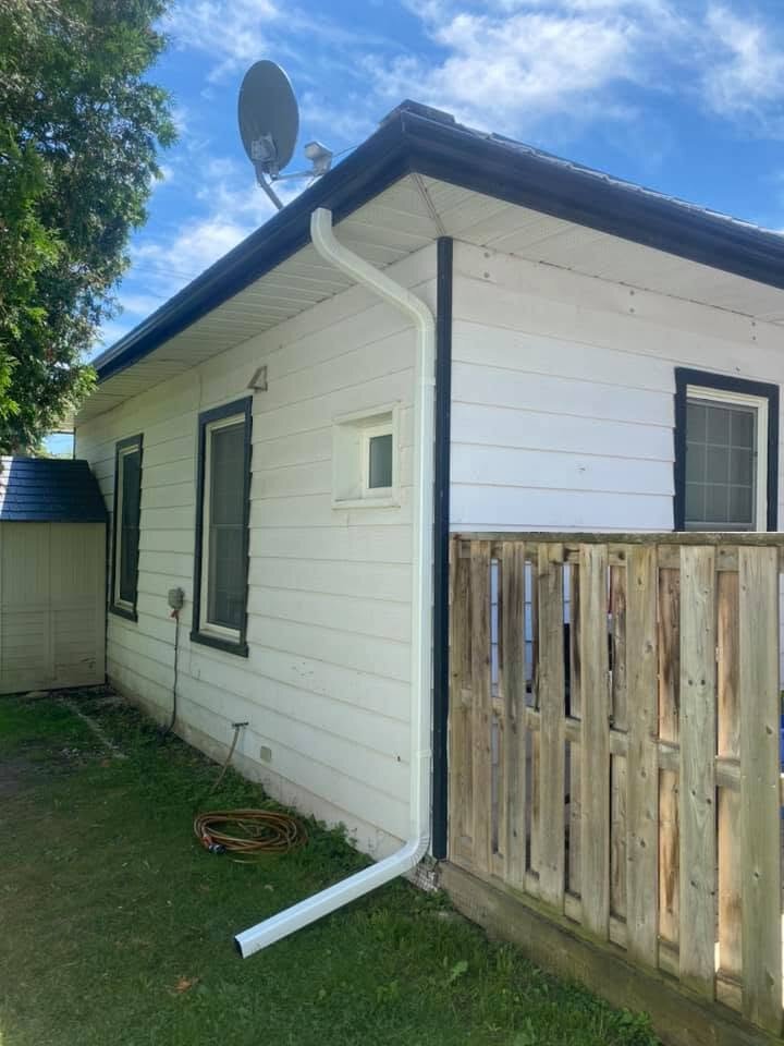 Rear addition with white siding and a new downspout beside a wood fence.